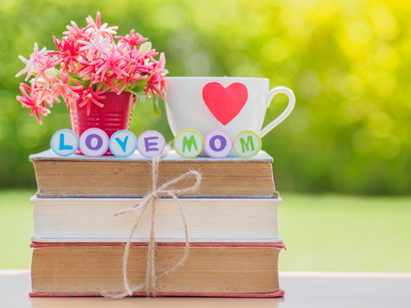 mother's day concept. LOVE MOM alphabet on stack of books, gifts, tea cup with red heart and flower on backgroundの写真素材