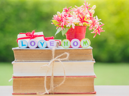 mother's day concept. LOVE MOM alphabet on stack of books, gifts, tea cup with red heart and flower on backgroundの写真素材