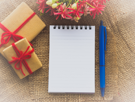 flower bouquet, gift and red flower, note book and blue pen on brown sack backgroundの写真素材