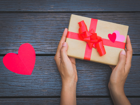 female hands holding a gift box on wooden table. Festive background for your design.の写真素材