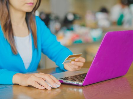 Pretty Young womans hands holding a credit card and using tablet, smartphone and laptop computer for online shopping. Online payment. Female working on smart phone laptop in a cafe.の写真素材