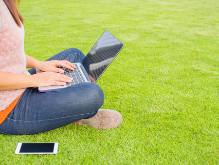 Pretty Young woman using laptop computer. Female working on laptop in an outdoor green grass fieldの写真素材