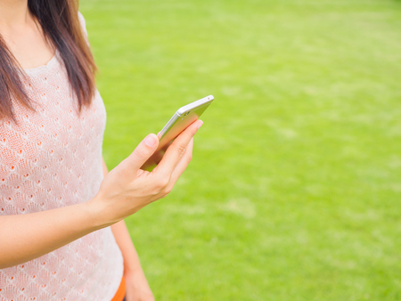 Pretty Young woman using smart phone. Female working on cell phone on green grass fieldの写真素材