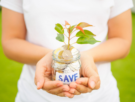 Women hand holding plant growing out of coins in glass jar on the green grass for money saving financial conceptの写真素材