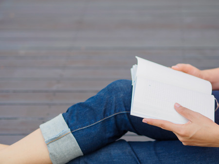 Woman with book sitting on wooden floorの写真素材