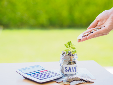 abstract money saving small baby tree with glass jar Coins with calculator on table with green tree backgroundの写真素材
