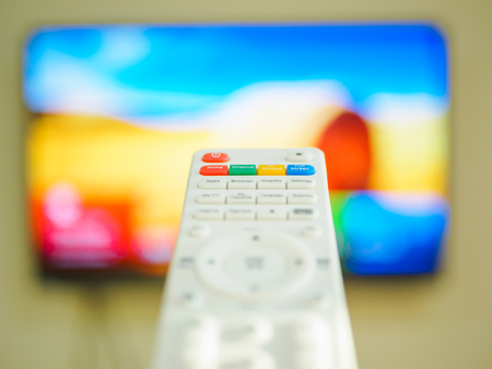 Close up Hand holding TV remote control with a television in the background.の写真素材