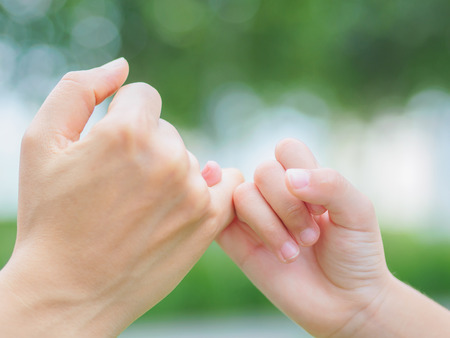 Mother holding a hand of her kid in spring day outdoors with green field backgroundの写真素材