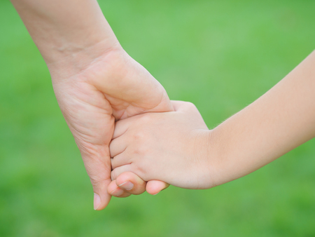 Mother holding a hand of her kid in spring day outdoors with green field backgroundの写真素材