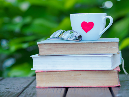 glasses and coffee white cup with red heart on stack of old booksの写真素材