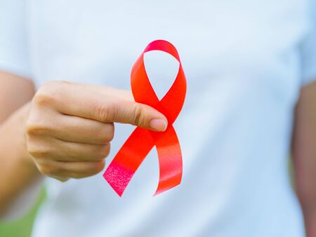 Red color ribbon awareness on young female woman girl teenager hand background: World aids day...