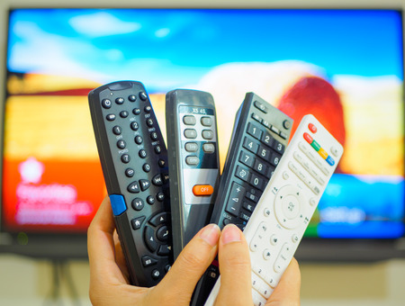 Close up Hand holding TV remote control with a television in the background.の写真素材