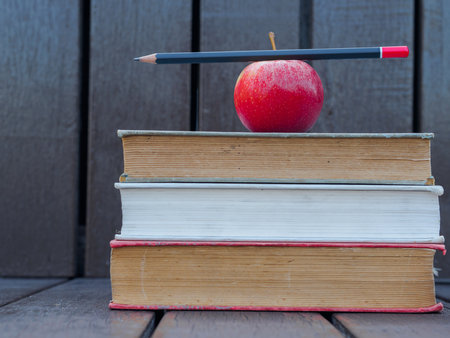 pencil put on red apple on stack of old booksの写真素材
