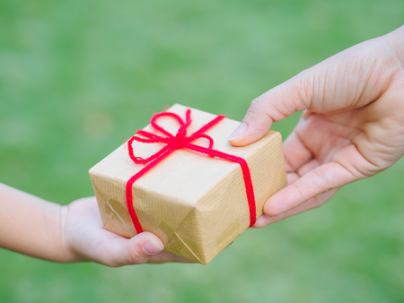 holidays, present, christmas, childhood and happiness concept - close up of child and mother hands with gift box over green backgroundの写真素材