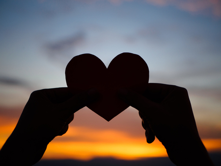 silhouette hand is raising the red paper heart with blur sunlight during sunset, Valentines dayの写真素材
