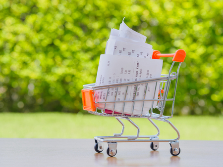 Shopping cart with receiptwith coins on wooden table, concept for grocery expenses and consumerismの写真素材