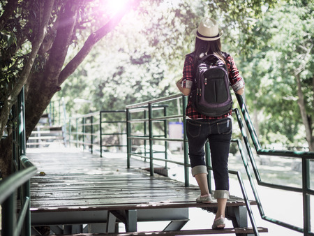 An Asian girl is hiking along the wooden trail bridge crossing into the jungle/forest in tropical area.の写真素材
