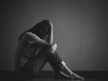 Black and white of sad woman hug her knee and cry. Sad woman sitting alone in a empty room.の写真素材