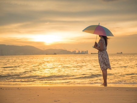 Lonely and depressed woman holding an umbrella and standing in front of the sea in a deserted beach on an Autumn day.の写真素材