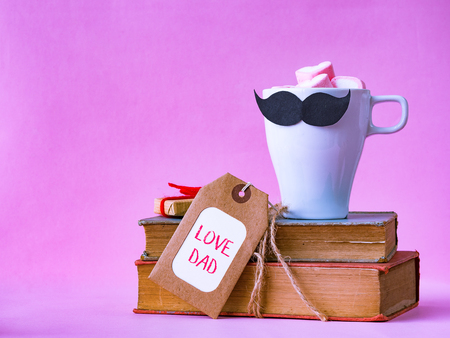 Father's day concept. LOVE DAD alphabet on stack of books, gifts, tea cup with black Mustache on pink backgroundの写真素材