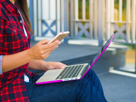 Pretty Young woman using smart phone. Female working on cell phone on green grass fieldの写真素材