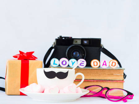Father's day concept. LOVE DAD alphabet on stack of books, gifts, glasses, retro camera, tea cup with black Mustache and  sweet marshmallow in the shape of heart on white backgroundの写真素材