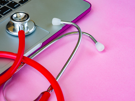 A medical stethoscope and a laptop on a pink table backgroundの写真素材