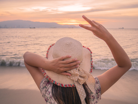 woman holds two fingers or Victory Sign on the beach during sunset, showing encouragement when we are discouraged.の写真素材