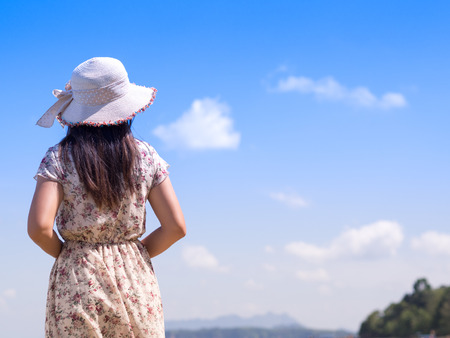 lonely Woman in summer vacation wearing straw hat and beach dress enjoying the view at the ocean alone.の写真素材