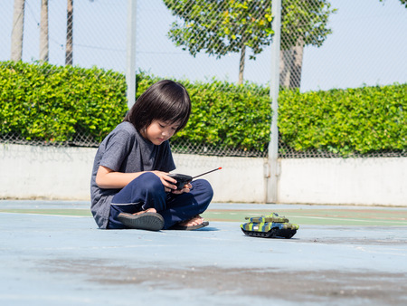 Adorable cute little child playing with toy tank, outdoors. Happy kid boy having fun on sunny summer day. Leisure, lifestyle for kids concept.の写真素材