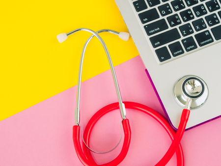 A medical stethoscope and a laptop on a pink and yellow table background. Education concept.の写真素材