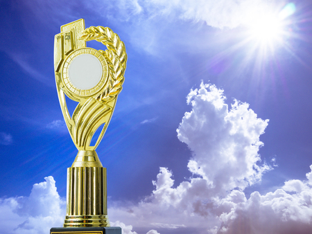 Golden award winning trophy on blue sky and sun backgroundの写真素材