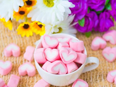 Closeup of sweet marshmallow in the shape of heart on wooden plate and flower at background. Concept about love and relationship. (Soft Style for Background)の写真素材