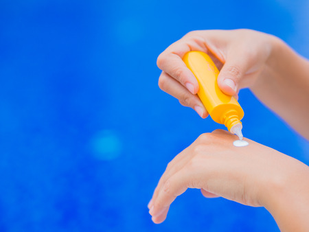 Woman hand apply sunscreen / sunblock by the swimming pool. Vacation and relaxation, summer travel concept.の写真素材