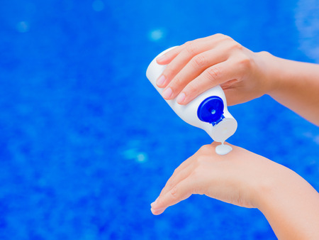 Woman hand apply sunscreen / sunblock by the swimming pool. Vacation and relaxation, summer travel...