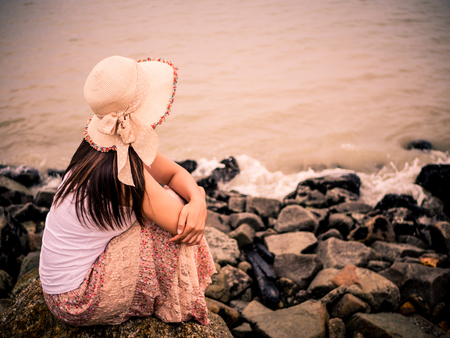 Retro lonely and depressed woman sitting in front of the sea in a deserted beach on an Autumn day.の写真素材