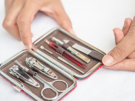Closeup woman hand holding traveler's nail care kit of necessary tools set including scissors, tweezers, nail file and trimmer in red leather pocket case.の写真素材