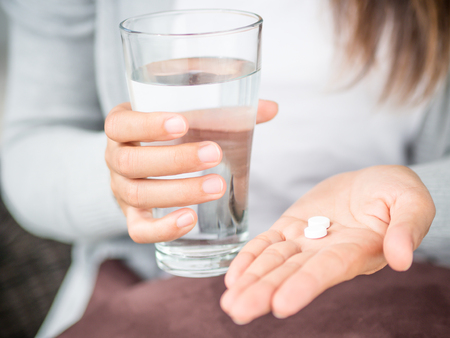 Closeup woman hand with pills medicine tablets and glass of water for headache treatment. Healthcare, medical supplements conceptの写真素材