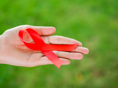 Closeup woman hand holding red ribbon HIV, world AIDS day awareness ribbon.  Healthcare and medicine...