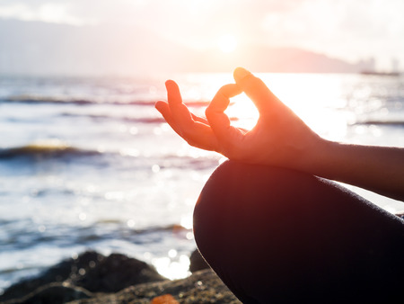 Yoga concept. Closeup woman hand practicing lotus pose on the beach at sunsetの写真素材