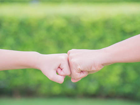 Closeup mother and son are fist bumping in green background. People, charity and family concept.