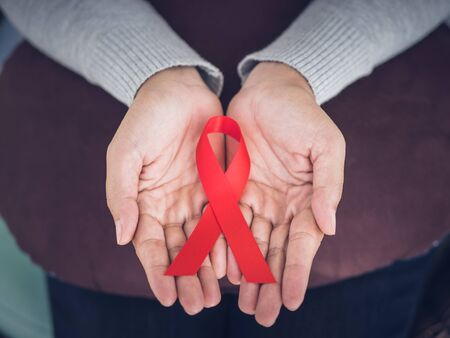 Closeup woman hands holding red ribbon HIV, world AIDS day awareness ribbon.  Healthcare and...