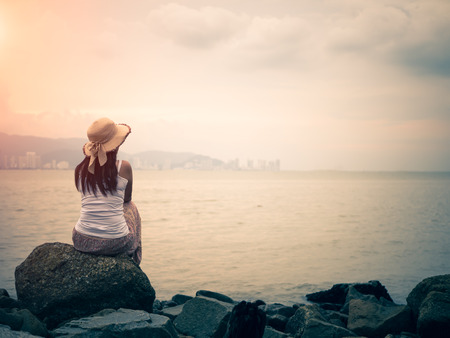 Retro style of lonely and depressed woman sitting in front of the sea in a deserted beach.の写真素材