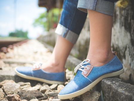 Closeup woman feet in blue sneakers sitting by the railway. Vacation and travel concept.の写真素材