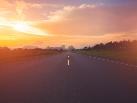 Old highway against mountains and a cloudy sky during sunset.