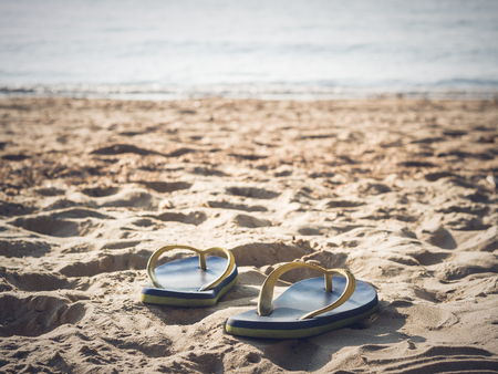 Soft focus at pair of flip-flops on the white sand beach with clear blue sea and sky,warm and vintage tone. Sad and hopeless concept.の写真素材