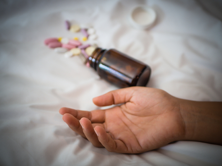 Closeup woman hand lying on the bed with pills. Drugs overdose or suicide concept.の写真素材