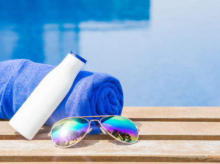 Sunglasses, blue towel and sunscreen at the side of swimming pool. Vacation, beach, summer travel conceptの写真素材