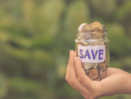 Retro abstract money saving women hand holding glass jar coins with green tree background.の写真素材