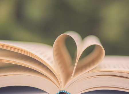Retro book on table in garden with top one opened and pages forming heart shape with selective focus.の写真素材